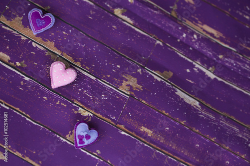 Сердечки из сиреневого/фиолетового и розового фетра ручной работы, вышитые бисером, на старом/вытертом деревянном полу 