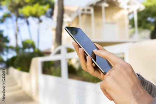 In the street woman using application on mobile phone. Blur nice house background photo