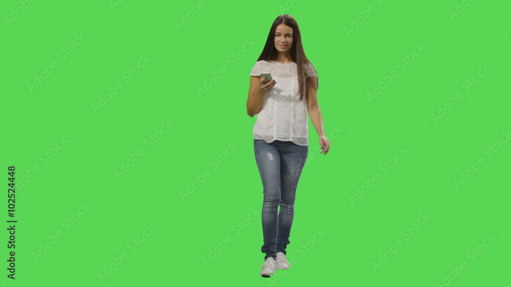 Casual brunette female is walking and using a smartphone on a mock-up green screen in the background. Shot on RED Cinema Camera. Casual brunette female is walking and using a smartphone on a mock-up green screen in the background. Shot on RED Cinema Camera.