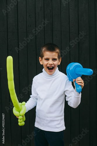 Boy playing with a balloon shape of sword in front of wooden door. 