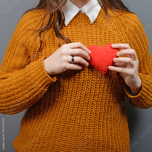 Beautiful happy woman holding heart in hands against gray backgr