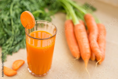 Fresh-squeezed carrot juice with vegetables on rustic background close up.