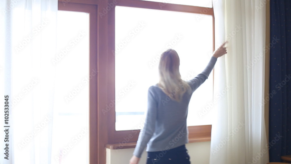 Beauty Girl opens curtains on big window and let the light in the room. Looking out the window. Beauty Girl opens curtains on big window and let the light in the room. Looking out the window.