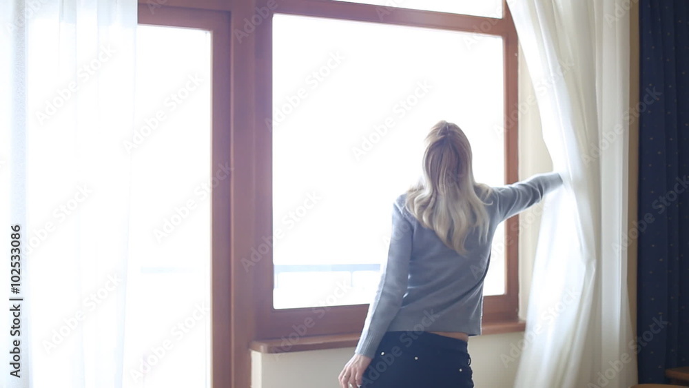 Beauty Girl opens curtains on big window and let the light in the room. Looking out the window Beauty Girl opens curtains on big window and let the light in the room. Looking out the window