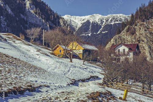 Fototapeta Naklejka Na Ścianę i Meble -  Sunny winter rural scenery with snowy Piatra Craiului mountain ridge, Romanian village and melting snow in Magura village, Brasov county, Romania.