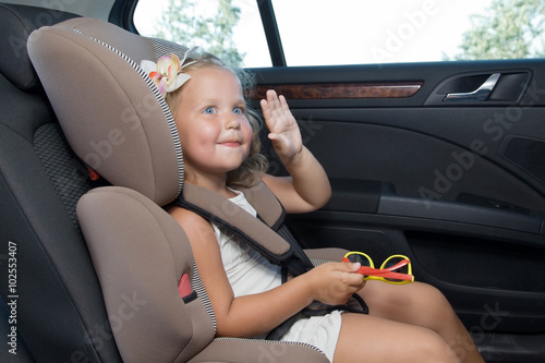 Little girl waves her hand sitting in car seat