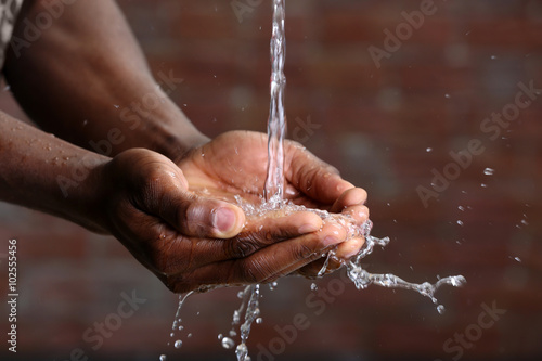 Hands washing concept. Water pouring into man hands on brick wall background