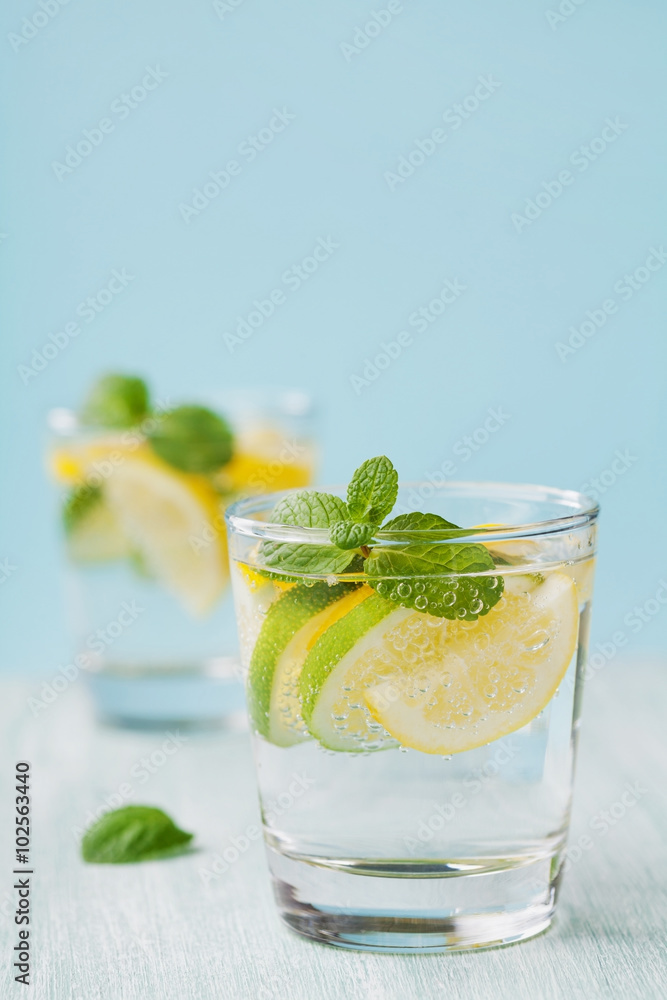 Mineral infused water with limes, lemons, ice and mint leaves on blue background, homemade detox soda water recipe Mineral infused water with limes, lemons, ice and mint leaves on blue background, homemade detox soda water recipe