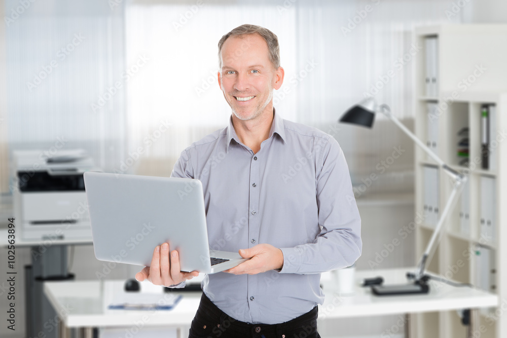Confident Businessman Holding Laptop In Office