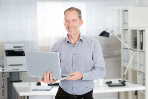 Confident Businessman Holding Laptop In Office