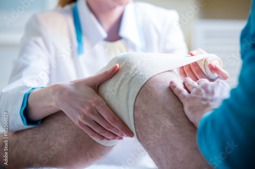 Female doctor is rewinding knee bandage to man. Doctor taking care of a patient with trauma of patella photo