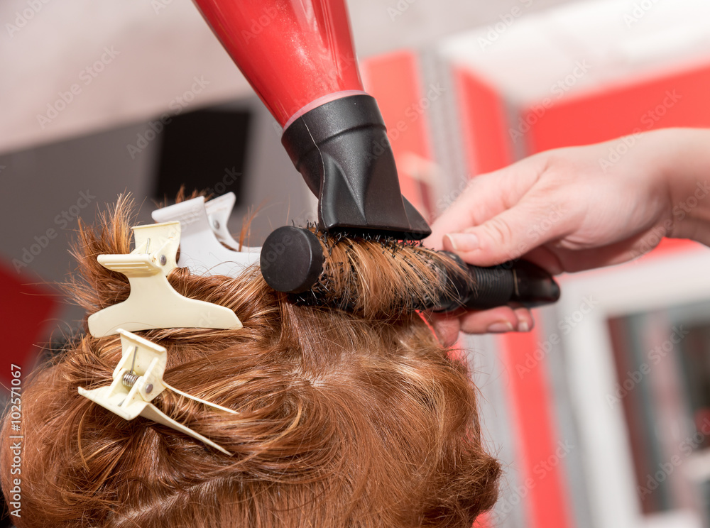 Fototapeta premium A hairdresser curling a lock with brush and drying a hairdryer. Selective focus.