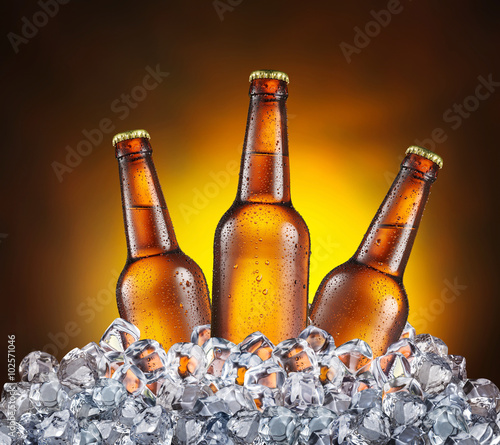 Three bottles of beer in the ice cubes on the yellow background.