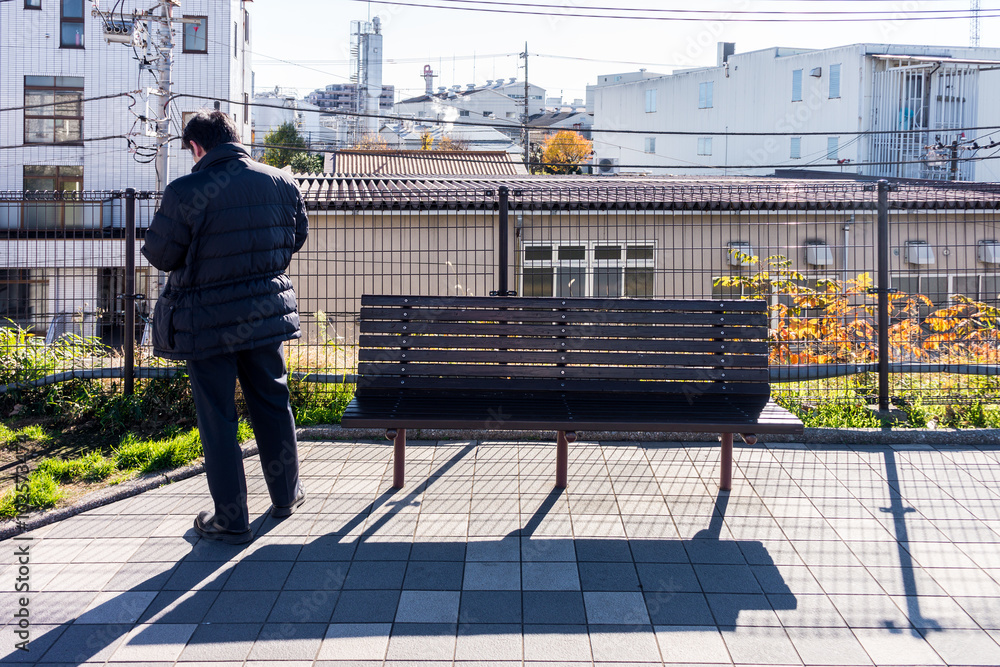 Asian man is waiting for someone nearby  wooden bench. The weather is cool in the morning.