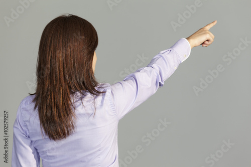 Back view of a business woman pointing finger on gray background