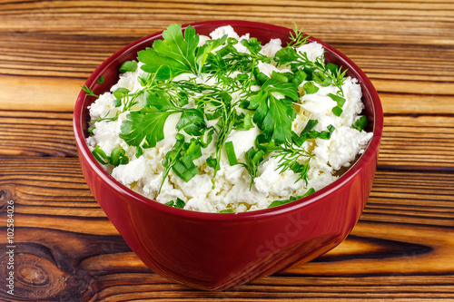 Fresh cottage cheese with sour cream, dill, parsley, onion in ceramic bowl on wooden table
