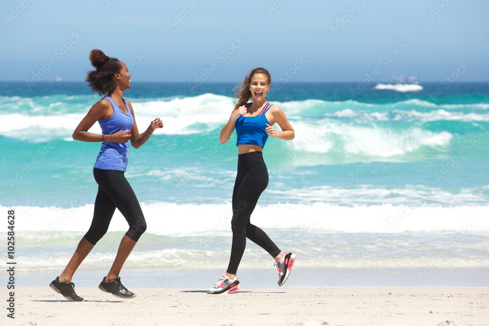 © mimagephotos - Two young women enjoying a run on the beach