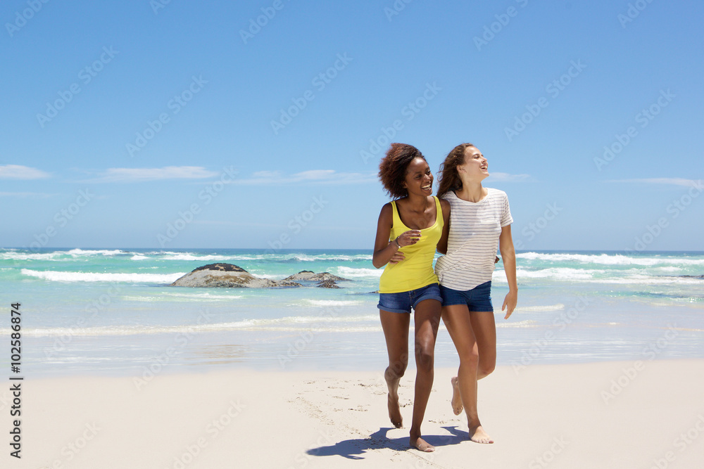 Female friends smiling and walking on the beach together