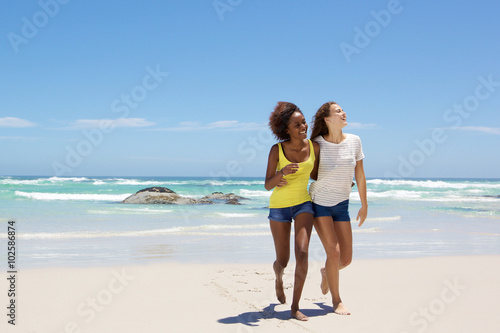 Female friends smiling and walking on the beach together