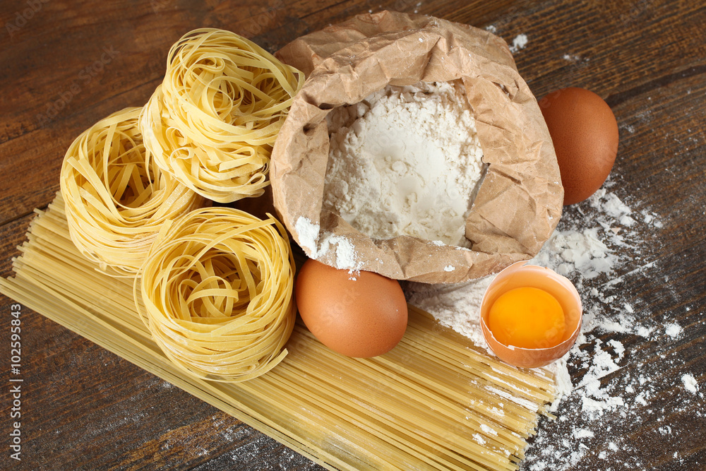 pasta with eggs, one of them broken and scattered flour with wooden spoon on brown wooden table