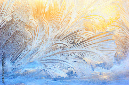 Window glass covered with ice pattern against sunset