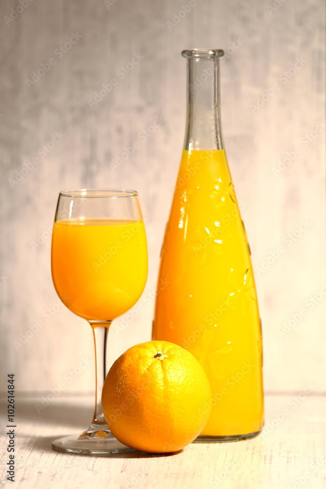 Fresh orange lemonade in a glass next to the whole fruit and orange slices on a light gray background. Selective focus Fresh orange lemonade in a glass next to the whole fruit and orange slices on a light gray background. Selective focus