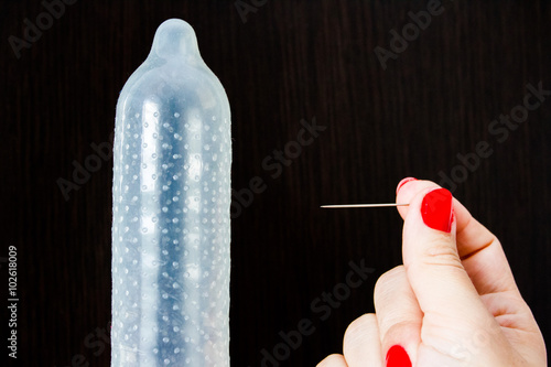 Inflated condom and a hand with a needle. Safe sex versus unprotected sex