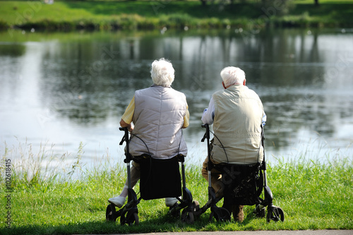 Zwei Rentner sitzen auf Rollatoren und sehen auf einen See.
