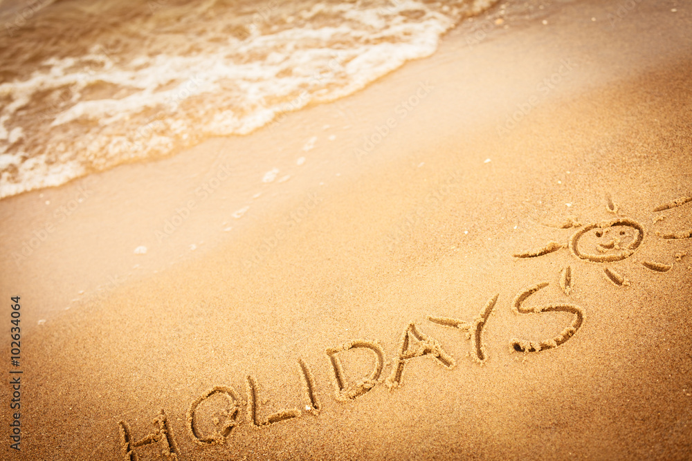 Fototapeta premium The word holidays written in the sand on a beach