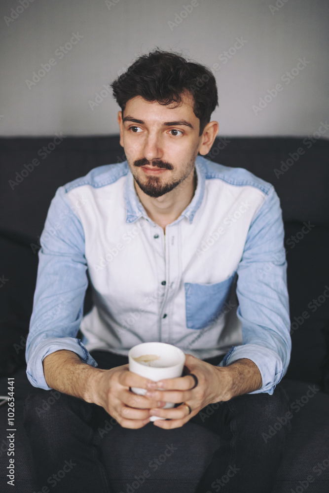 Handsome casual man sitting on couch having coffee Handsome casual man sitting on couch having coffee