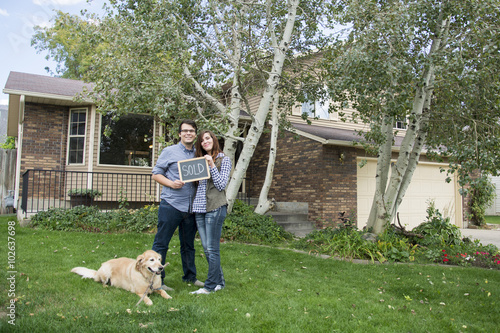 couple and dog in front of new home with sold sign