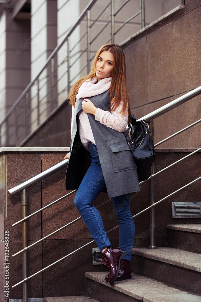 Young fashion woman in grey coat with handbag on the steps