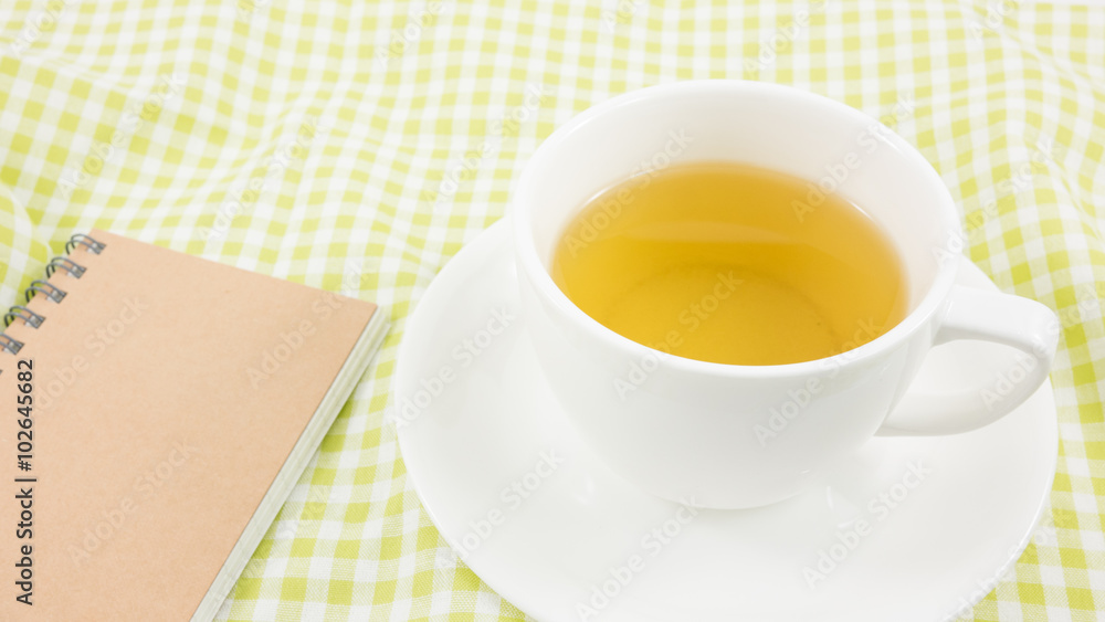 The cup of Japanese green tea and small note book on green cotton fabric. The cup of Japanese green tea and small note book on green cotton fabric.
