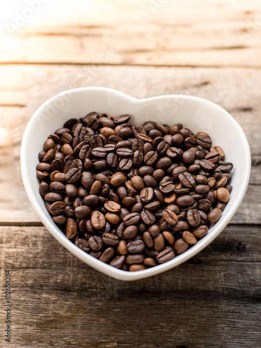 coffee bean in a bowl in the form of heart on a wooden backgroun