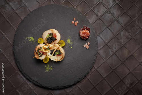 фотографія Haute cuisine scallops served on black plate. Top view.