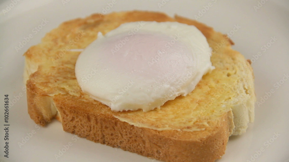Placing a poached egg on toast then slicing with a knife with yolk oozing out. Placing a poached egg on toast then slicing with a knife with yolk oozing out.