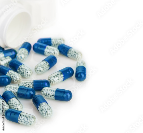 Blue capsules, pills poured out of a white bottle close-up on a white background.