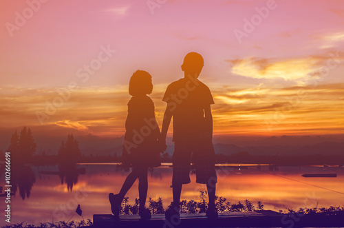 Brother and sister holding hands together with sun set.