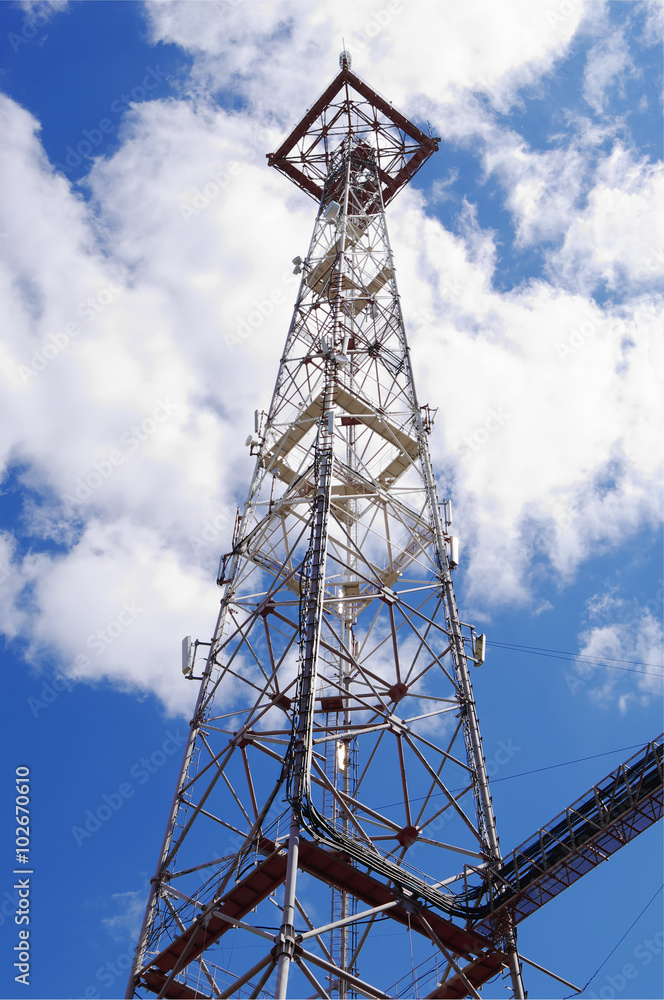 top part of communication tower with antennas closeup on blue clouds sky 