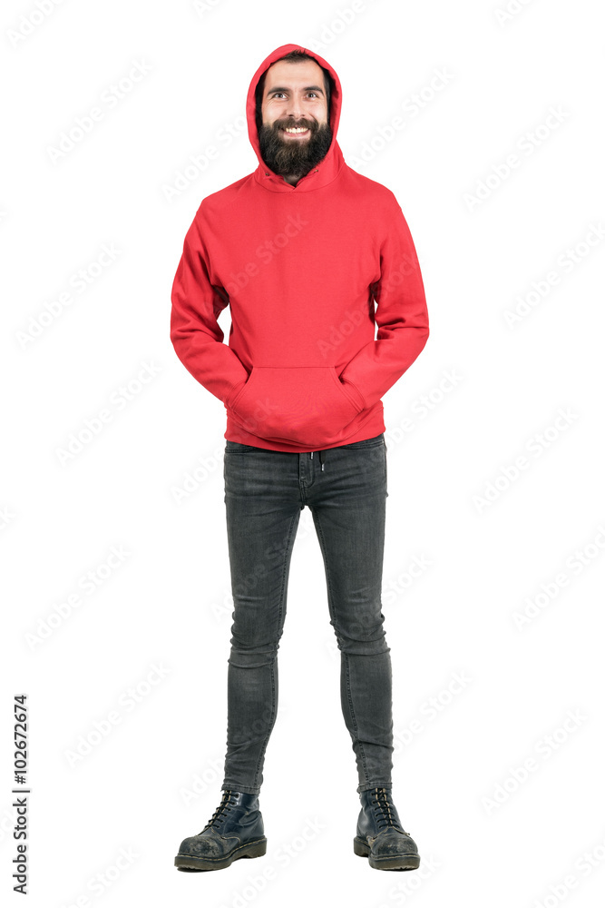 Laughing bearded punker wearing red hoodie looking at camera with hands in pockets. Full body length portrait isolated over white studio background. Laughing bearded punker wearing red hoodie looking at camera with hands in pockets. Full body length portrait isolated over white studio background.