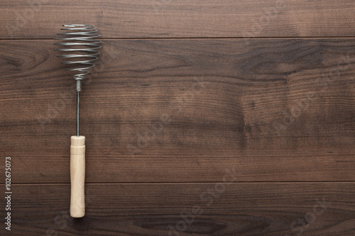 retro egg whisk with wooden handle on brown table with copy space