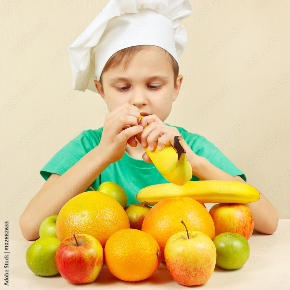 Little chef peeling fresh banana at the table with fruits Little chef peeling fresh banana at the table with fruits