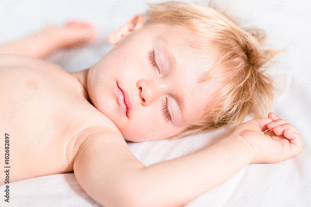 Close-up portrait of handsome toddler boy with blond hair sleeping on white bed. Carefree childhood concept Close-up portrait of handsome toddler boy with blond hair sleeping on white bed. Carefree childhood concept
