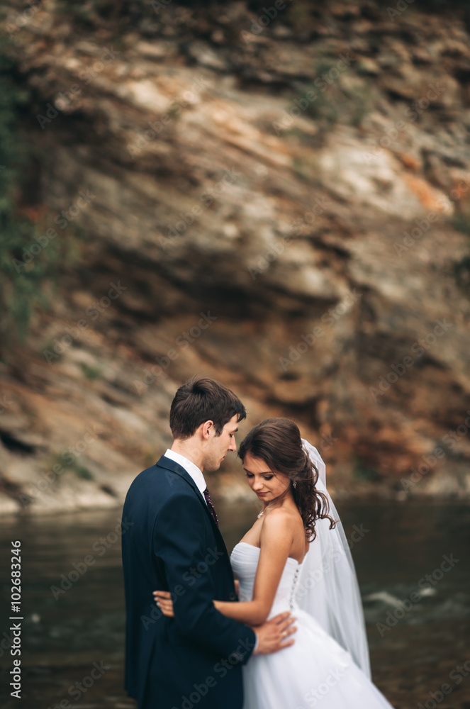 Naklejka premium Elegant gentle stylish groom and bride near river with stones. Wedding couple in love