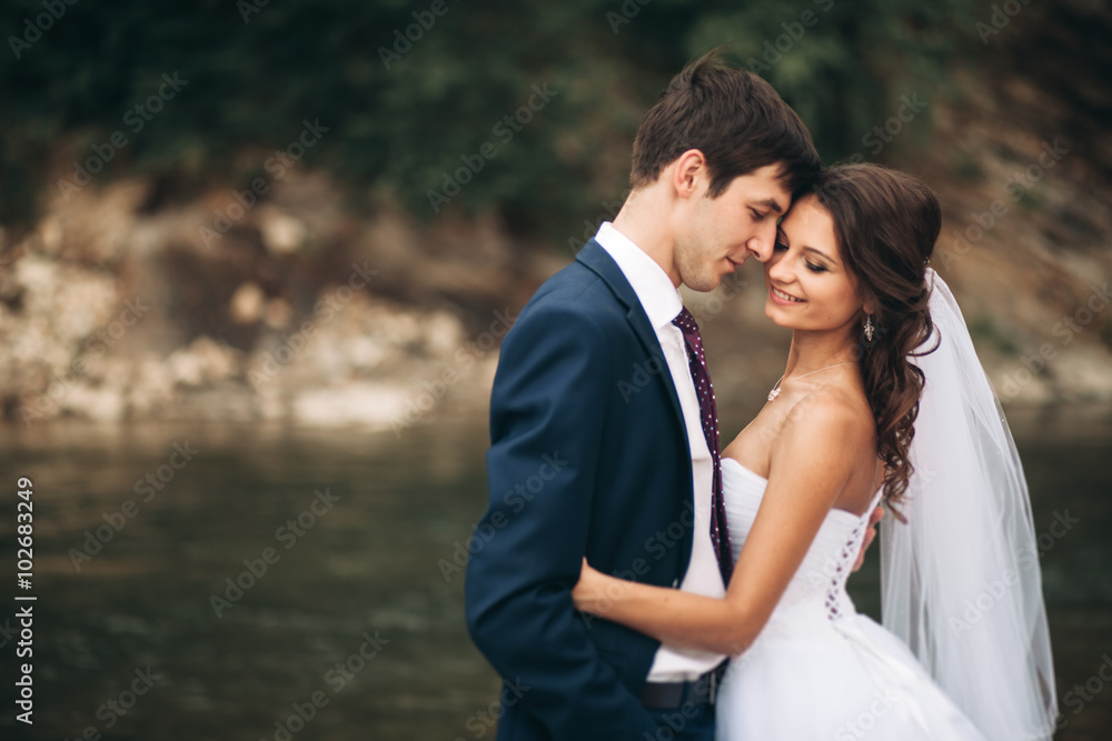 Elegant gentle stylish groom and bride near river with stones. Wedding couple in love Elegant gentle stylish groom and bride near river with stones. Wedding couple in love