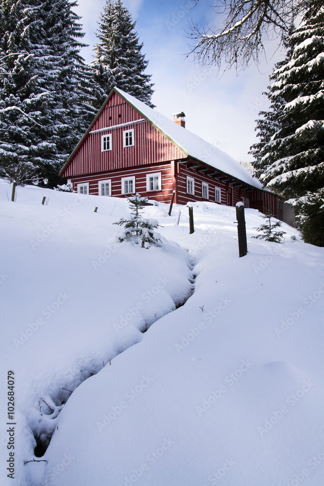 Red wooden cabin in a frosty snowy country in sunny winter day