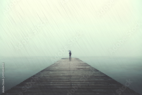 Quadro su tela Sad man with umbrella on a boardwalk under rain