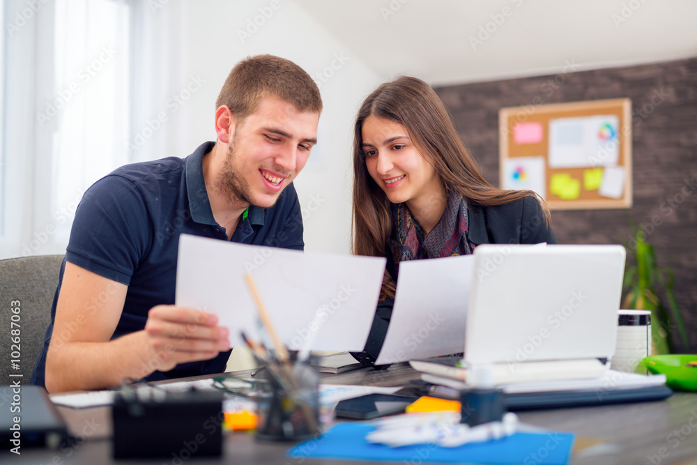 Beautiful smiling young businesswoman sitting working with a young man in a busy office Beautiful smiling young businesswoman sitting working with a young man in a busy office