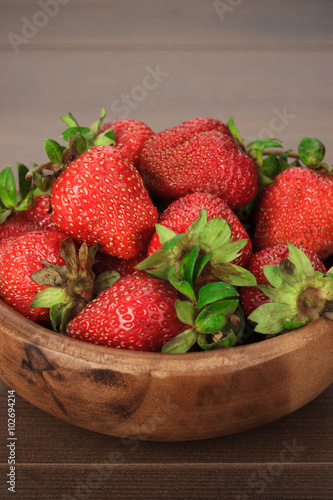 wooden bowl full of fresh strawberries on the brown table