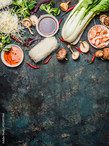 Asian cooking ingredients: rice noodles, pok choy , sauces, shrimps, chili and Shiitake mushrooms on dark background, top view, place for text. Asian food concept: Chinese or Thai cuisine.